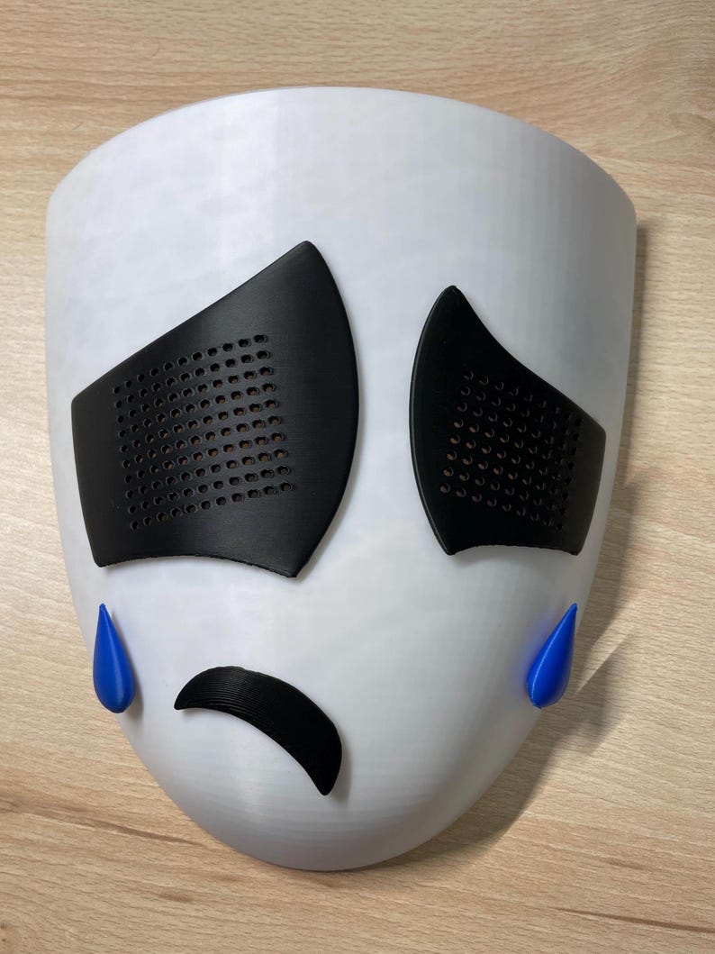 May include: White plastic mask with black eyes, a black frown, and blue teardrop shapes on the sides.