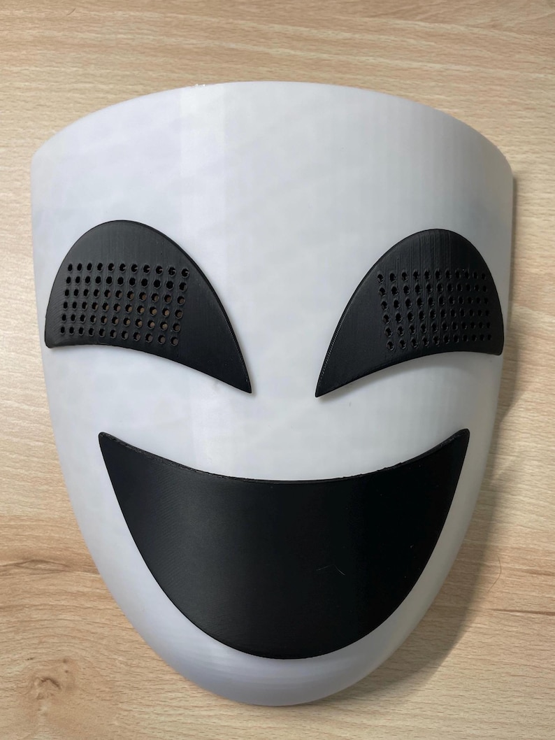 May include: A white plastic mask with a black smiling mouth and two black eyes with a grid pattern.