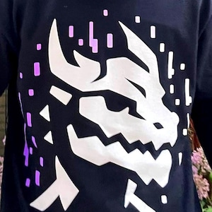 May include: Black long-sleeved shirt with a white graphic of a dragon's head with a pixelated design in purple.