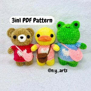 Puede incluir: Tres juguetes de peluche de crochet: un oso marrón, un pato amarillo y una rana verde. Cada juguete lleva una camisa rosa, marrón o azul con un corazón blanco y una bolsa a juego. El texto "3in1 PDF Pattern" está por encima de los juguetes y "@n.y_arts" está por debajo de los juguetes.