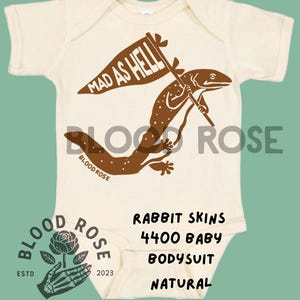 May include: Cream-colored baby bodysuit with a brown lizard graphic holding a flag that reads "MAD AS HELL." The text "BLOOD ROSE" and "RABBIT SKINS 4400 BABY BODYSUIT NATURAL" are also printed on the bodysuit.
