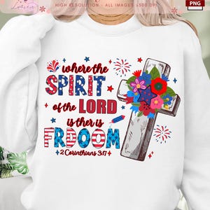 Puede incluir: Sudadera blanca con un diseño gráfico rojo, blanco y azul que presenta una cruz con flores, fuegos artificiales y el texto "Where the Spirit of the Lord is there is Freedom" y "2 Corinthians 3:17".