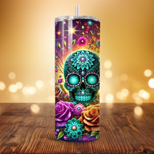 May include: A tall, stainless steel tumbler with a colorful Day of the Dead design. The design features a teal skull with floral accents, surrounded by roses and other flowers in shades of purple, orange, and teal. The background is a gradient of purple and gold.