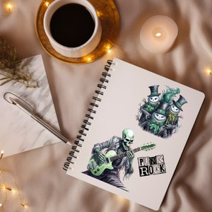 Op de afbeelding: Een notitieboek met twee stickers. E&eacute;n sticker toont een skelet dat een groene elektrische gitaar bespeelt met de tekst "Punk Rock". De andere sticker toont drie groene sneeuwpoppen met zwarte hoeden.