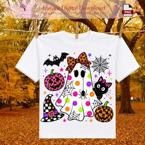 以下が含まれることがあります： カラフルなハロウィンのグラフィックがプリントされた白いTシャツ。ヒョウ柄のリボンをつけたゴースト、黒猫、チェック柄の魔女の帽子、ヒョウ柄とチェック柄の2つのカボチャ、クモ、クモの巣、小さな星が描かれています。