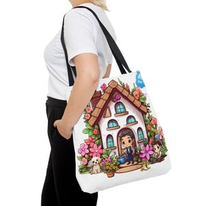 K&ouml;nnte beinhalten: Eine wei&szlig;e Einkaufstasche mit einer Cartoon-Illustration eines Hauses mit braunem Dach, Blumen und zwei Personen. Das Haus hat blaue Fenster und eine wei&szlig;e T&uuml;r. Die Personen halten Gartenger&auml;te. Die Tasche hat schwarze Henkel.