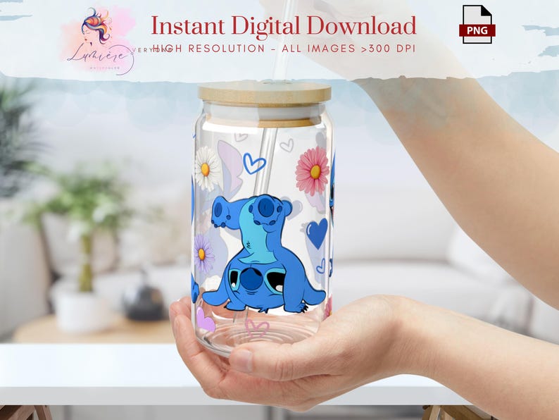 Op de afbeelding: Een heldere glazen tumbler met een bamboe deksel en een blauw cartoonfiguur met een rietje. De tumbler heeft een bloemenontwerp met roze en witte bloemen en harten.