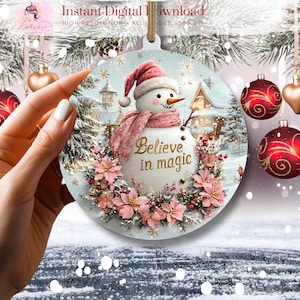 May include: A round Christmas ornament with a snowman in a pink scarf and hat, surrounded by pink flowers and the words "Believe in magic".