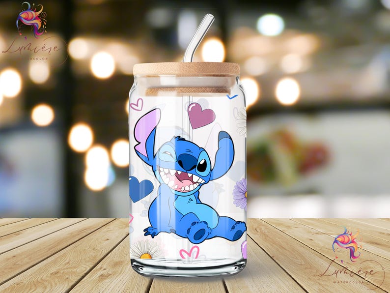 Op de afbeelding: Een transparante glazen beker met een blauw en paars cartoonfiguur erop. Het figuur is Stitch uit de Disney-film Lilo & Stitch. De beker heeft een rietje en een houten deksel. De achtergrond is wazig en onscherp.