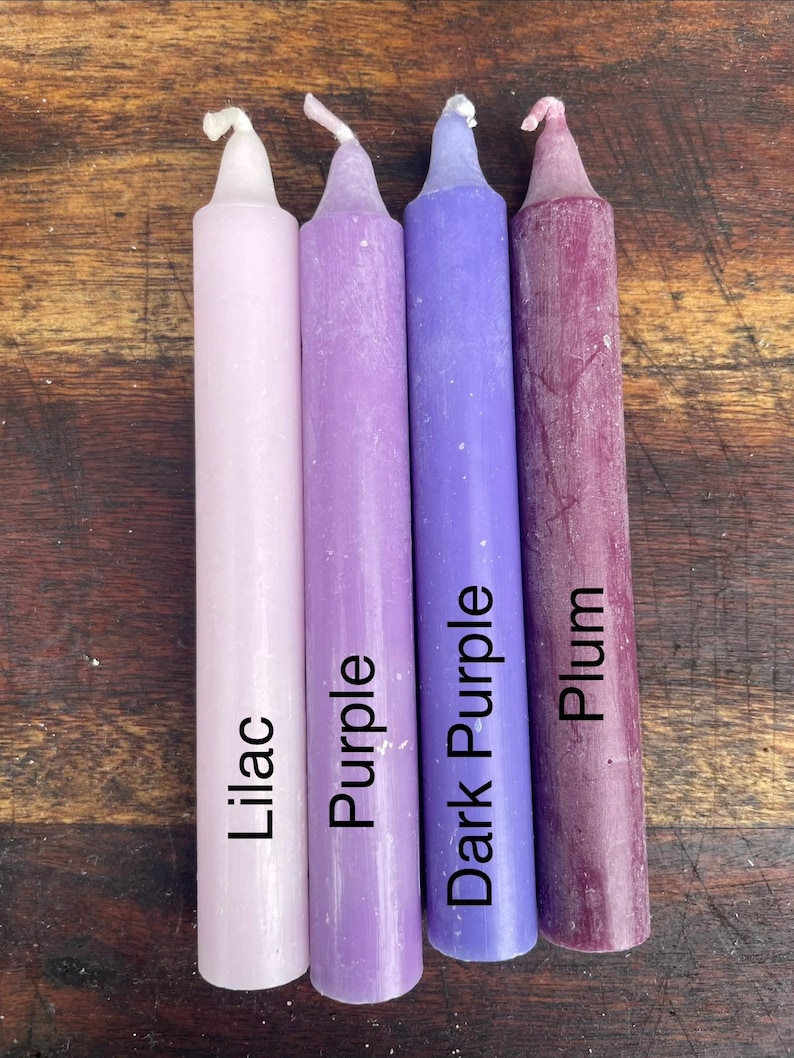 Może przedstawiać: Cztery cylindryczne świece stożkowe ustawione obok siebie w gradiencie odcieni fioletu. Świece są oznaczone napisami Lilac, Purple, Dark Purple oraz Plum, odpowiadającymi ich kolorom od najjaśniejszego do najciemniejszego.