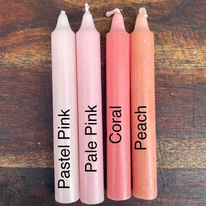 Może przedstawiać: Cztery cylindryczne świece stożkowe ustawione obok siebie. Świece mają nadrukowany tekst na swoich powierzchniach: Pastel Pink, Pale Pink, Coral oraz Peach. Każda świeca ma spiczastą g&oacute;rę i gładkie wykończenie z wosku w jednolitym kolorze.