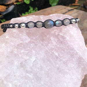 Puede incluir: Un brazalete de cordón negro con cuentas plateadas y cuentas de piedra lunar grises.