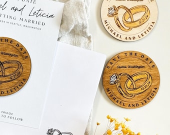 May include: A white paper card with black text reading Save the Date, Michael and Leticia, and Getting Married in Seattle, Washington, alongside three circular wooden magnets engraved with the same names, date 12.21.24, and ring graphics.