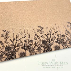 Puede incluir: Un corcho personalizado con un borde floral grabado. El diseño presenta flores y follaje negros en el borde inferior. El logotipo de Dusty Wise Man es visible. Ideal para mostrar notas y fotos.