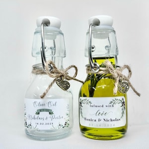 Puede incluir: Dos peque&ntilde;as botellas de vidrio con tapones de corcho y detalles de cuerda. Una botella est&aacute; llena de aceite de oliva y tiene una etiqueta que dice "Infundido con amor Monica & Nicholas 02.14.2024". La otra botella est&aacute; vac&iacute;a y tiene una etiqueta que dice "Aceite de oliva con amor Nicholas & Portia 14.02.202X".