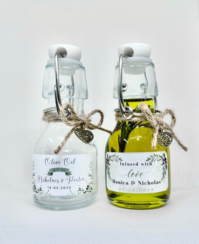 Puede incluir: Dos peque&ntilde;as botellas de vidrio con tapones de corcho y detalles de cuerda. Una botella est&aacute; llena de aceite de oliva y tiene una etiqueta que dice "Infundido con amor Monica & Nicholas 02.14.2024". La otra botella est&aacute; vac&iacute;a y tiene una etiqueta que dice "Aceite de oliva con amor Nicholas & Portia 14.02.202X".