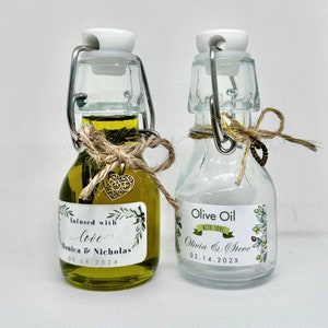 Puede incluir: Dos peque&ntilde;as botellas de vidrio con aceite de oliva. Las botellas tienen etiquetas con un dise&ntilde;o de hojas verdes y el texto "Infused with love Monica & Nicholas 02.14.2024" y "Olive Oil with love Olivia & Steve 02.14.202X".