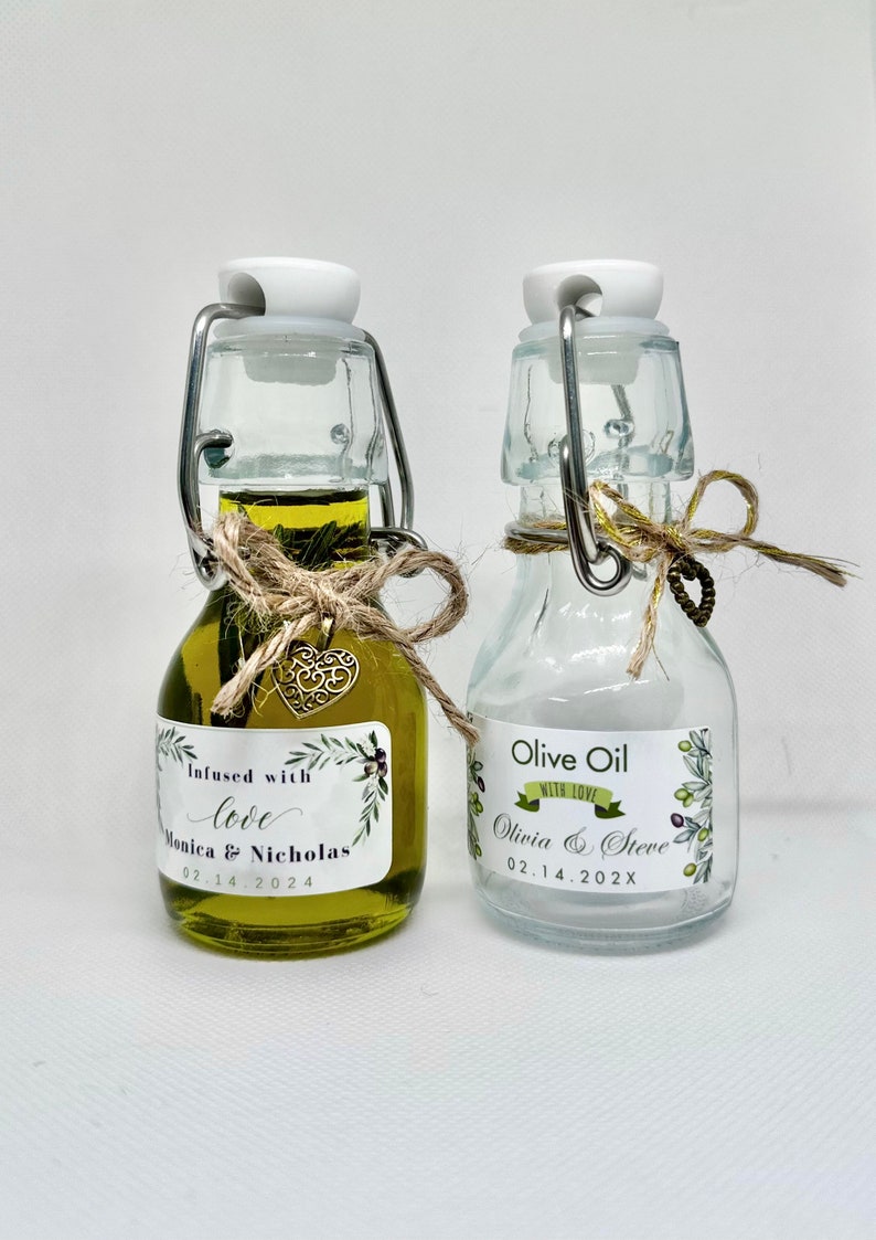 Puede incluir: Dos peque&ntilde;as botellas de vidrio con aceite de oliva. Las botellas tienen etiquetas con un dise&ntilde;o de hojas verdes y el texto "Infused with love Monica & Nicholas 02.14.2024" y "Olive Oil with love Olivia & Steve 02.14.202X".