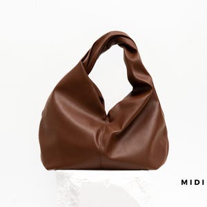 May include: A brown leather handbag with a twisted handle. The bag has a soft, slouchy design and is displayed against a white background. The word "MIDI" is printed in black on the bottom right.