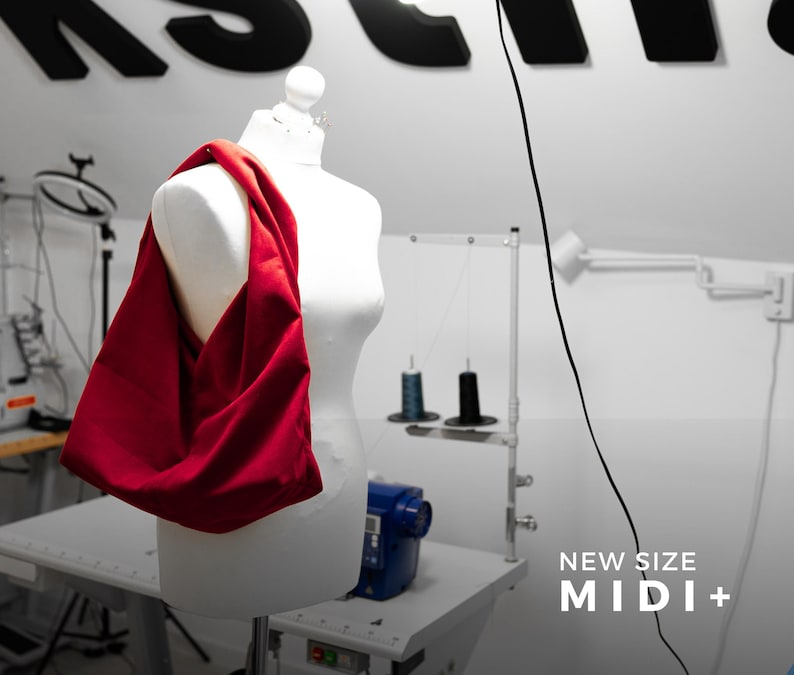 May include: A red fabric bag draped over a white mannequin. The bag is a solid, vibrant red. The background includes a sewing machine, spools of thread, and the text "NEW SIZE MIDI+".