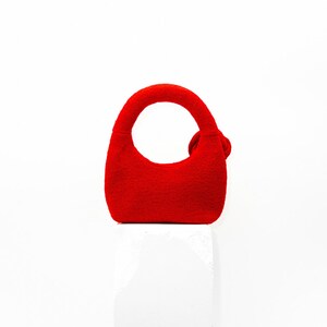 May include: A small, bright red handbag with a rounded handle and a small decorative accent. The bag is made of a textured material and sits on a white surface. The bag's design is simple and modern.