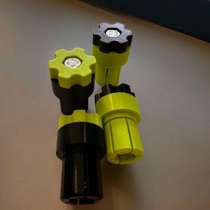 Könnte beinhalten: Vier schwarz- und limettengrüne 3D-gedruckte Objekte. Jedes Objekt hat eine zahnradförmige Oberseite mit Metalleinsatz, einen zylindrischen Körper und eine geschlitzte Basis. Auf den limettengrünen Oberteilen steht "SRS B.B".