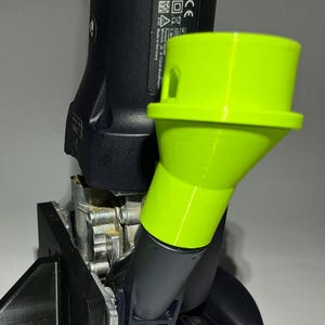 Puede incluir: Una herramienta eléctrica negra y gris con un accesorio de embudo verde brillante. La herramienta tiene una marca CE y el texto "Made in Germany". El embudo está en ángulo y parece estar impreso en 3D.