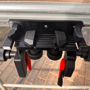 Può includere: Morsetto nero stampato in 3D con due leve rosse e due manopole nere. Il morsetto è fissato a una guida argentata.