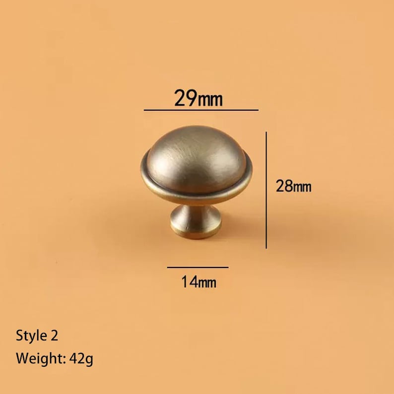 May include: Antique brass-finished cabinet knob, Style 2, with a rounded top and a pedestal base. The knob measures 29mm wide, 28mm high, and 14mm deep. It weighs 42g. The knob is designed for furniture hardware.