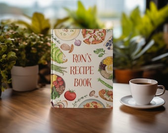 May include: A white cookbook with a colorful illustration of various foods on the cover. The title of the book is "Ron's Recipe Book" in red text.