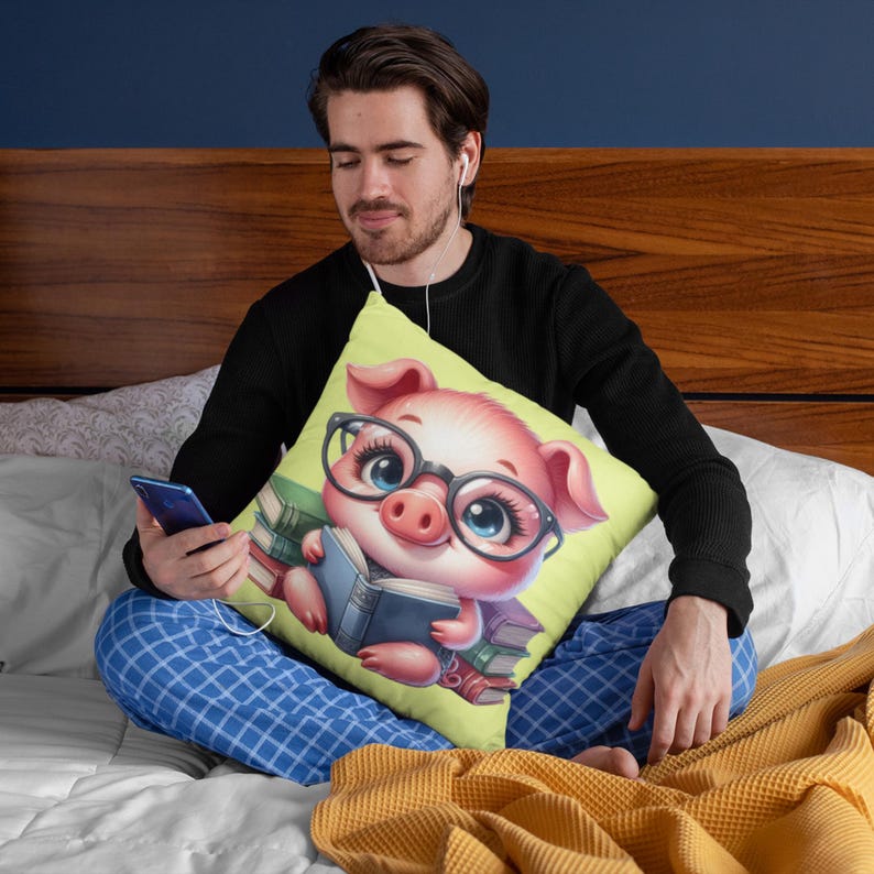 A man is sitting on a bed, wearing headphones and holding a cell phone. He is resting his head on a pillow featuring a cartoon pig wearing glasses and reading a book.