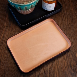 Könnte beinhalten: Ein hellbraunes Ledertablett mit einem dunkelbraunen Rand. Das Tablett liegt auf einer Holzoberfläche.