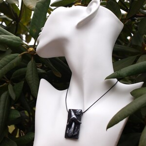 Puede incluir: Un collar negro con un colgante que presenta un diseño de hongo esculpido. El colgante está hecho de arcilla polimérica y tiene un acento plateado.