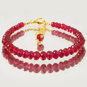 Peut inclure: Un bracelet composé de perles circulaires facettées d'un rouge profond. La pièce présente un fermoir mousqueton en métal doré et une chaînette d'extension réglable qui se termine par une perle rouge assortie au bout de la chaîne.