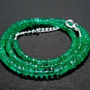 May include: A necklace composed of numerous small, faceted, vibrant green gemstone beads arranged in a circular pattern. The necklace features a polished silver-toned metal lobster claw clasp and a short length of silver-toned metal chain extender.