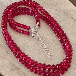 May include: A multi-strand necklace featuring faceted, deep red beads arranged in a circular pattern. The necklace includes a silver-toned metal lobster claw clasp and a short silver-toned metal extender chain with small links for adjustable length.