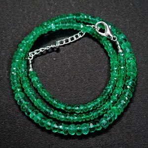 May include: A necklace composed of numerous small, faceted, vibrant green gemstone beads arranged in a circular pattern. The strand features a silver-toned metal lobster claw clasp and an adjustable chain link extension for securing the jewelry.