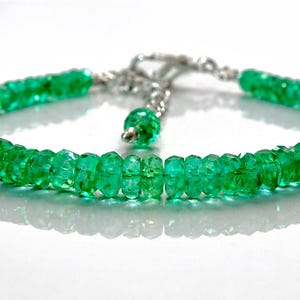 Puede incluir: Un brazalete de esmeraldas verdes. El brazalete está compuesto por cuentas de esmeralda facetadas ensartadas, con un cierre plateado y una cuenta de esmeralda colgante. Las cuentas son de un verde rico y translúcido.