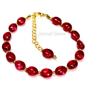 May include: A bracelet featuring oval-shaped, translucent red beads separated by small, round gold-toned metal spacers. The piece includes a gold-toned metal chain extender with a lobster clasp and the text Jannat Gems printed in the centre.