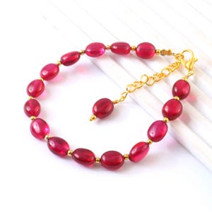 Peut inclure: Un bracelet composé de perles ovales rouge foncé translucides alternant avec de petites perles d'espacement rondes de couleur or métallique. Le bijou comprend une chaînette d'extension dorée avec un fermoir mousqueton et une perle rouge assortie.