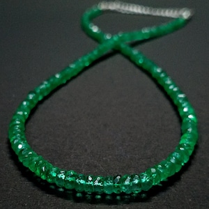 May include: A necklace composed of small, faceted, vibrant green gemstone beads arranged in a circular pattern. The strand features a metallic silver-toned extender chain at the top, providing an adjustable closure for the circular beaded necklace.