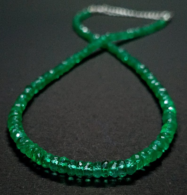 May include: A necklace composed of small, faceted, vibrant green gemstone beads arranged in a circular pattern. The strand features a metallic silver-toned extender chain at the top, providing an adjustable closure for the circular beaded necklace.