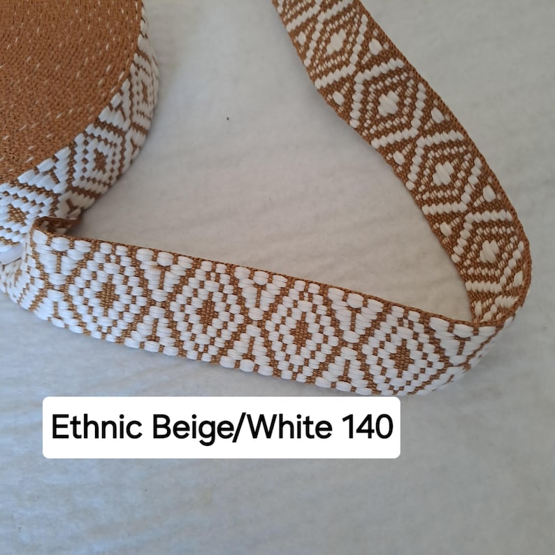 Op de afbeelding: Close-up van een beige en wit patroonlint. Het lint heeft een herhalend geometrisch diamantontwerp. De tekst "Ethnic Beige/White 140" is zichtbaar. Dit lint is geschikt voor knutsel- of naaiprojecten.