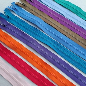 May include: A selection of colourful zippers in shades of pink, red, orange, purple, blue, and green. The zippers are arranged diagonally, displaying their different colours and metal zipper pulls. Suitable for sewing and craft projects.