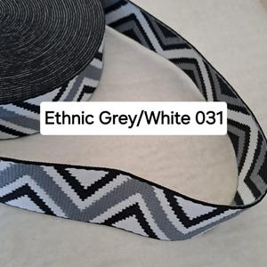 Op de afbeelding: Een rol elastisch lint met een zwart-wit patroon en een zigzagontwerp. Het lint heeft een herhalend patroon van zwarte, grijze en witte zigzags. De tekst "Ethnic Grey/White 031" staat op het lint.