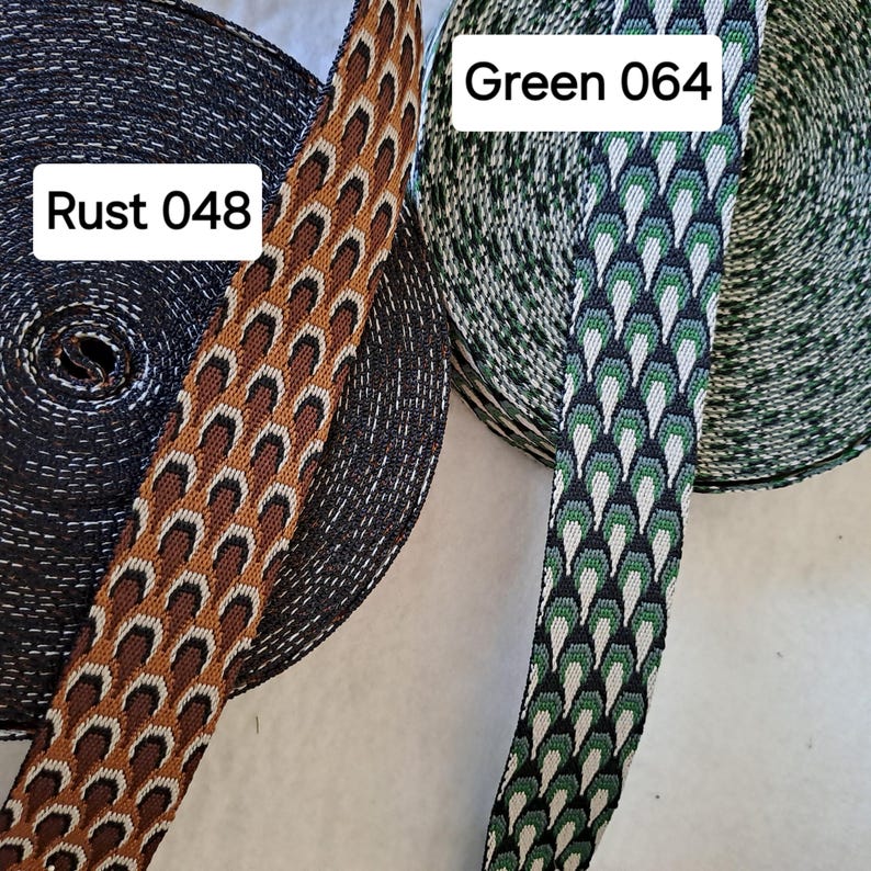 Op de afbeelding: Close-up van twee spoelen decoratief lint. E&eacute;n spoel is zwart met een roestkleurig lint met een herhalend patroon, met het label "Rust 048". De andere spoel is groen met een geometrisch patroonlint, met het label "Green 064".