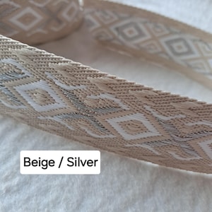 Op de afbeelding: Close-up van een beige en zilveren geweven lint. Het lint heeft een herhalend ruitpatroon in witte en zilveren draad. De tekst "Beige / Silver" staat in een witte rechthoek. Geschikt voor knutselen of decoratie.