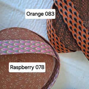 Op de afbeelding: Twee spoelen decoratief lint. E&eacute;n spoel is oranje met een zwart en grijs geometrisch patroon. De andere spoel is bruin met een roze en groen geometrisch patroon. Tekst op de afbeelding luidt "Orange 083" en "Raspberry 078".