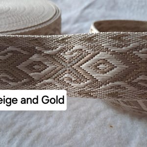 Op de afbeelding: Beige en goud geweven lint met een geometrisch ruitpatroon. Het lint is opgerold in een spoel, met een gedeelte afgerold om het gedetailleerde ontwerp te laten zien. De tekst "Beige and Gold" wordt op de afbeelding weergegeven.