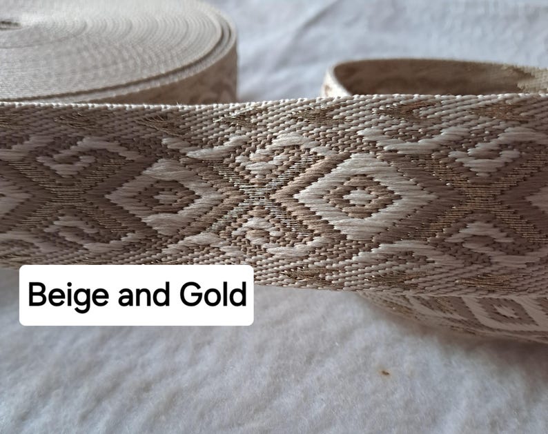 Op de afbeelding: Beige en goud geweven lint met een geometrisch ruitpatroon. Het lint is opgerold in een spoel, met een gedeelte afgerold om het gedetailleerde ontwerp te laten zien. De tekst "Beige and Gold" wordt op de afbeelding weergegeven.